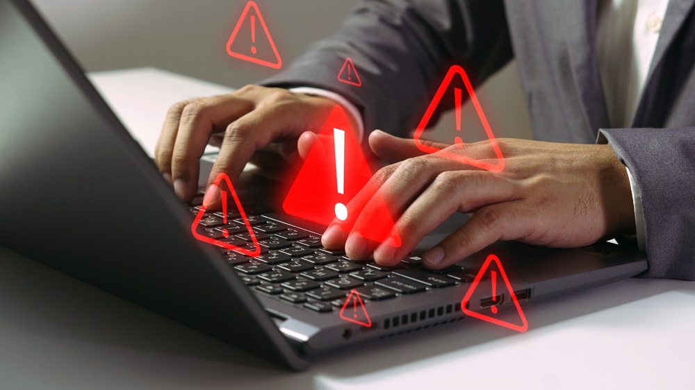 Hands typing on a laptop keyboard as red warning triangles with exclamation marks float above the keys.